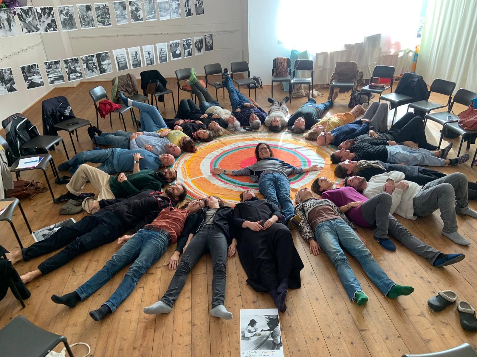 Un gruppo di adulti sdraiati in cerchio attorno a un mandala colorato